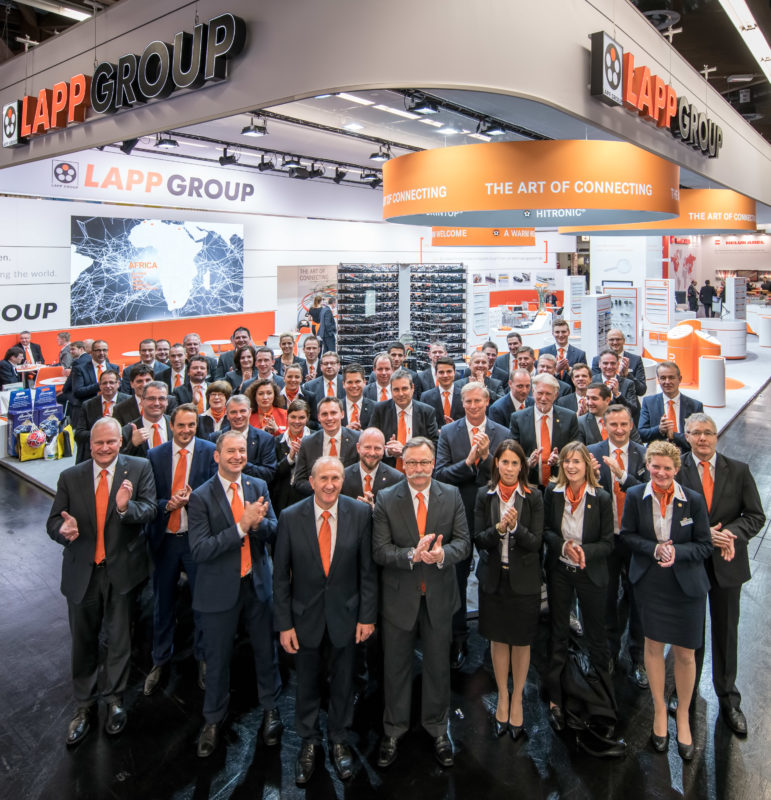 Group photo: Portrait of the entire stand personnel for the appearance of a company at an international trade fair. In the background you can see the entire exhibition stand.