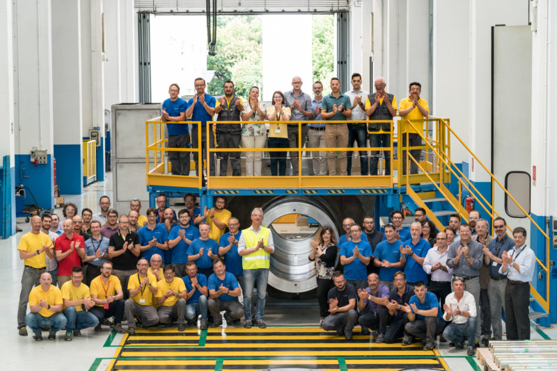 Group photo: Employees of a metalworking company in one of the factory buildings. Everyone wears goggles and claps.