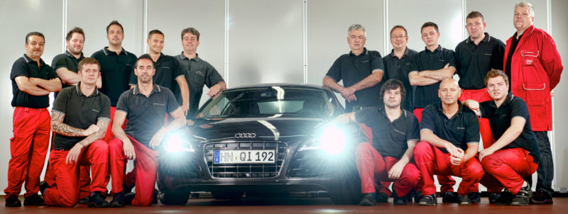 Group photo: A group of employees surround the vehicle on which they work.