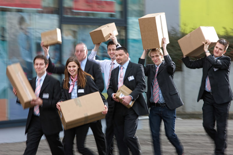 Gruppenfoto: Die Mitarbeiter eines Telekom Shops tragen Kartons mit Waren zu ihrem Laden.