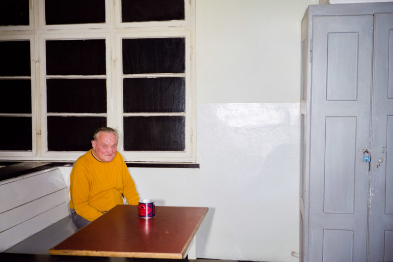 Reportagefotografie bei der Heilsarmee: Ein bedürftiger älterer Mann sitzt im dürftigen Aufenthaltsraum bei der Heilsarmee und wartet, dass er an die Reihe kommt.
