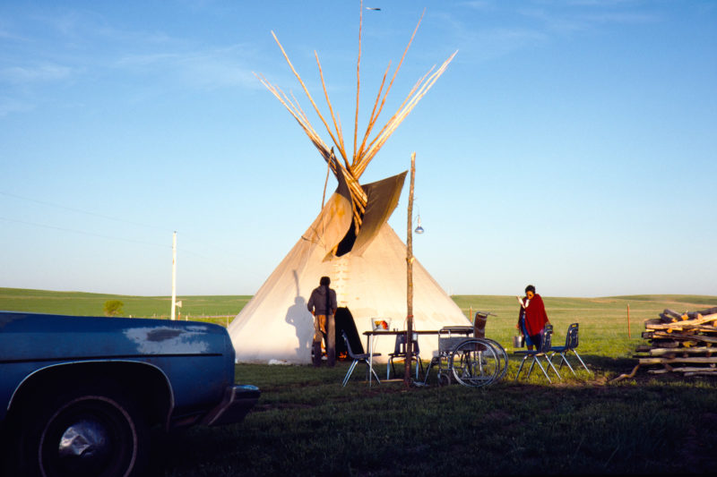 Reportagefotografie auf Diafilm in der Pine Ridge Reservation in South Dakota, USA: Eine Frau trägt mit Adlerfeder in der Hand Wasser in das Zelt, in dem gerade eine Schwitz-Zermenonie beginnt.