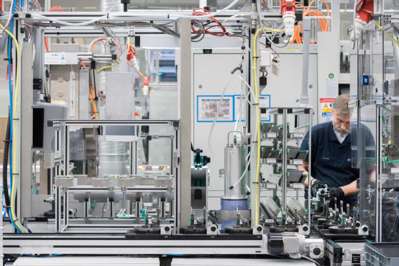 Industrial photography: An industrial employee prepares parts for series production in a semi-automatic production plant. He wears black gloves to protect himself from the sharp edges.