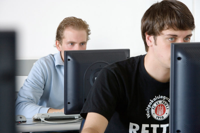 Reportagefotografie: Zwei Schüler einer weiterführenden Schule beim Informatikunterricht. Sie sitzen mit konzentriertem Blick hinter den Bildschirmen, so dass man Mund und Nase nicht mehr sehen kann.