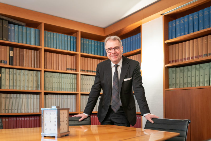 Interview photos: Portraits during a conversation with an economic expert. The interviewee stands relaxed in the library and smiles into the camera.