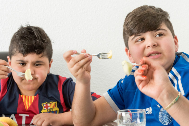 Editorial photography, subject learning and education: Two younger brothers while eating fruit at home at the family table.