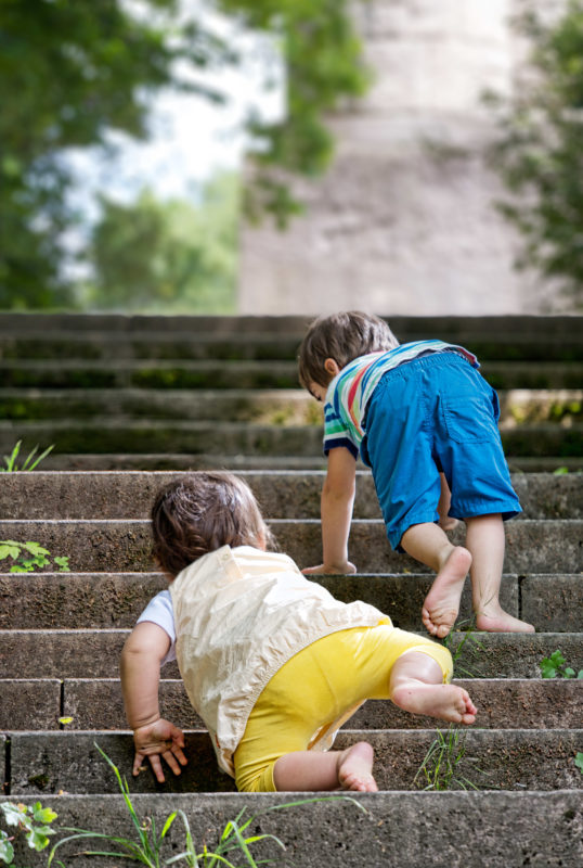 Editorial photography: As his older brother a small child attempts to climb a staircase.