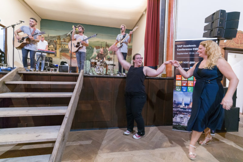 Reportagefotografie als Eventfotografie und Messefotografie: Am Abend einer mehrtägigen Konferenz tanzen Teilnehmerinnen ausgelassen an der Bühne zu der Musik einer Band.