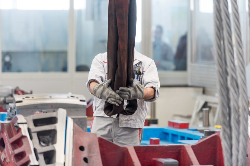 Industrial photography: In an assembly hall, an employee pulls the heavy lifting-straps of an overhead crane.