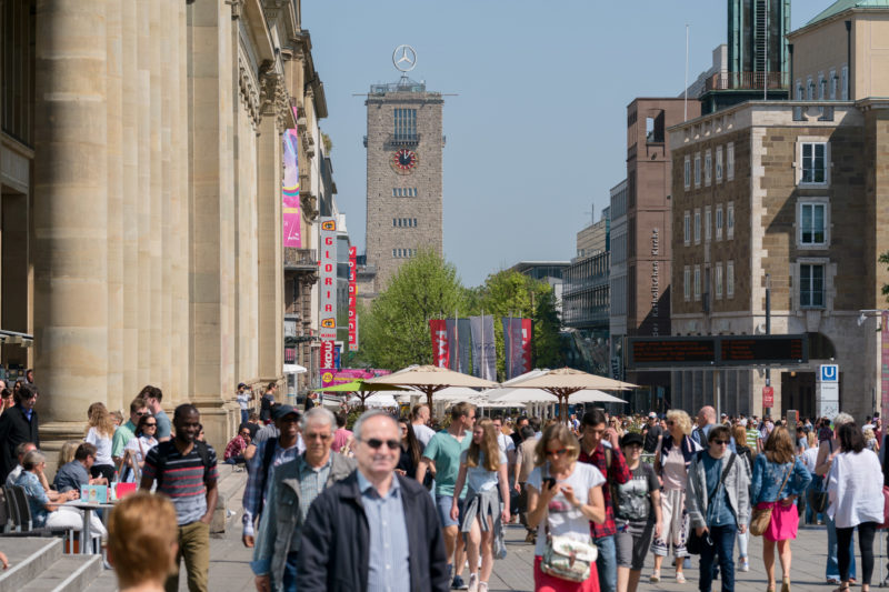 Stadtportrait Stuttgart: Stadtansicht der dicht bevölkerten Fussgängerzone Königstraße in Stuttgart. Das Foto wurde mit einem Teleobjektiv aufgenommen. So überragt der weit entfernte Bahnhofsturm die Szene.