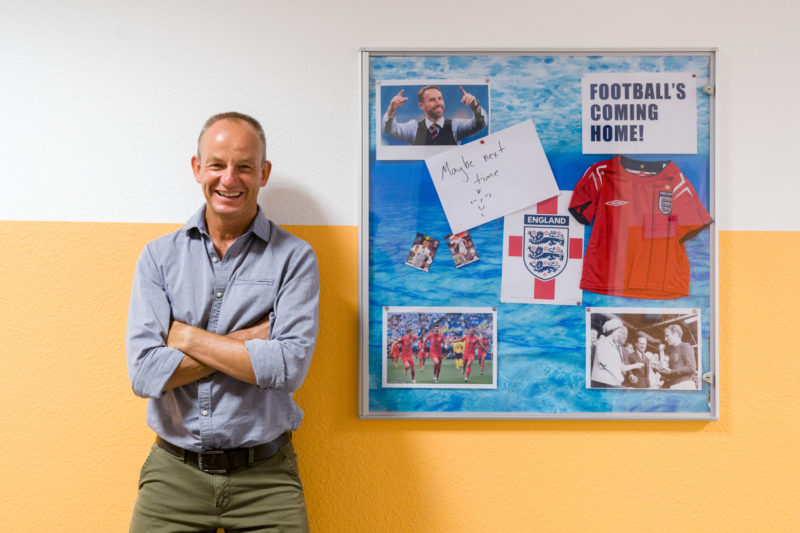 Reportagefotografie: Ein Lehrer bei der Arbeit: Auf dem Flur in der Schule hängt für den Englischunterricht eine Collage zum Thema englischer Fussball. 