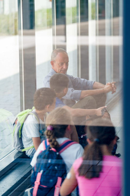 Editorial photography: A teacher at work: During a break, the teacher sits on the floor in the hallway together with some of the students and talks to them.