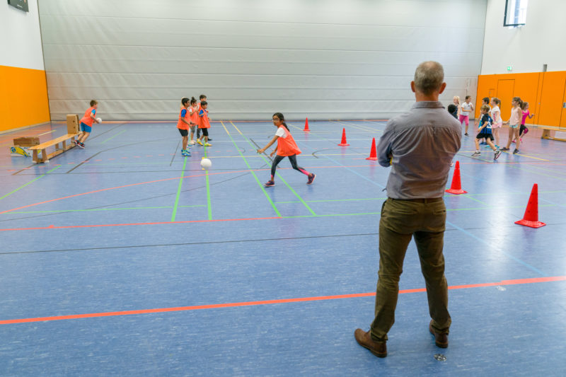 Reportagefotografie: Ein Lehrer bei der Arbeit: Er beobachtet beim Sportunterricht als Schiedsrichter das Völkerballspiel der Kinder.