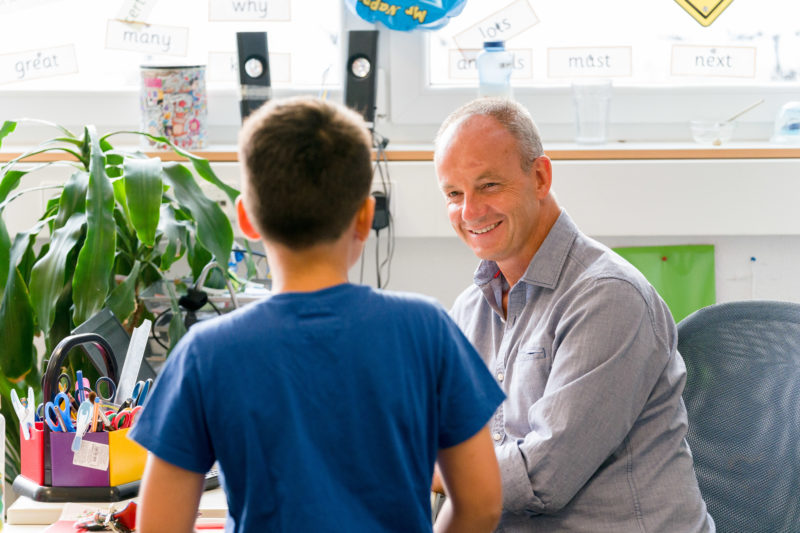 Reportagefotografie: Ein Lehrer bei der Arbeit: Er freut sich, als ein Schüler zu ihm kommt und ihn um Rat fragt.