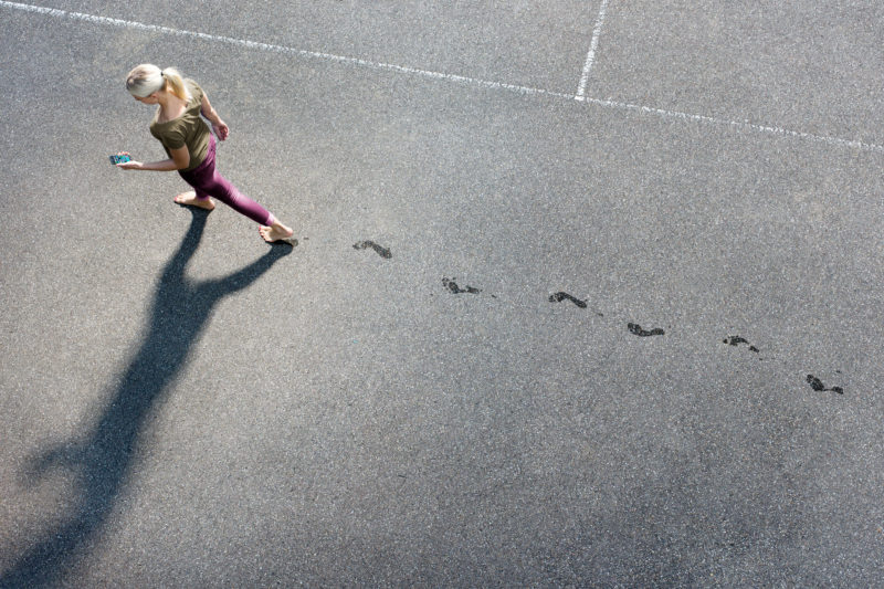 Lifestyle-Fotografie: Ein Mann läuft mit seinem Smartphone in der Hand barfuß über Asphalt.