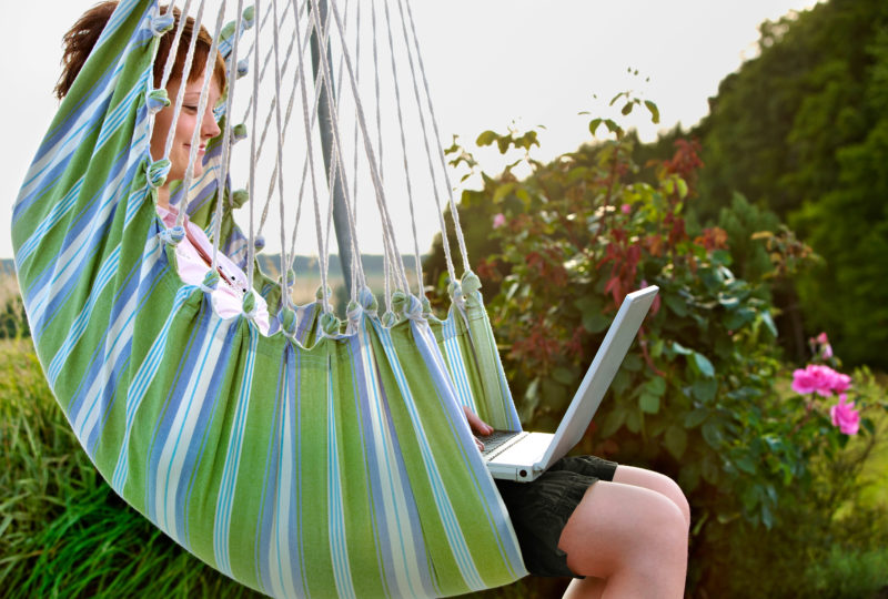 Lifestyle photography: A girl in a hammock surfs the Internet with her laptop.