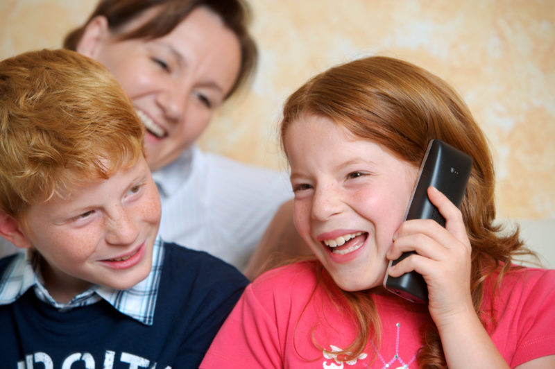 Lifestyle photography: The daughter phones at home assisted by her brother and her mother.