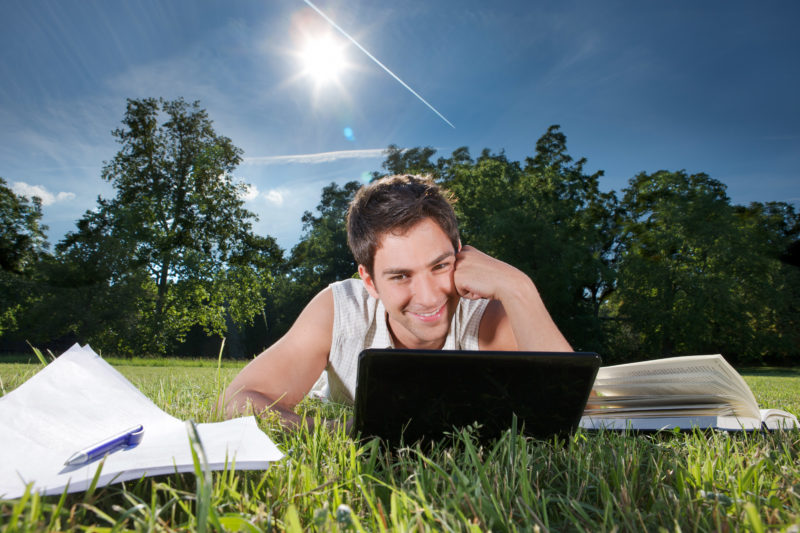 Lifestyle photography: A student works in the grass with the netbook online.