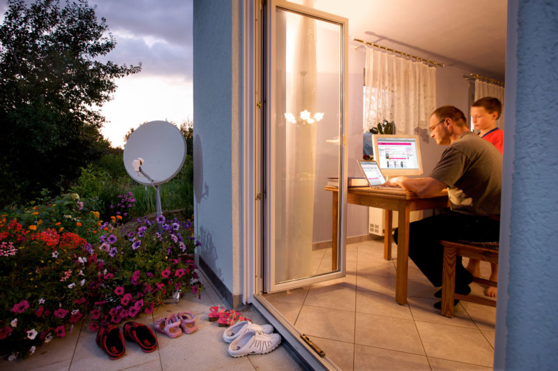 Lifestyle-Fotografie: Ein Vater surft gemeinsam mit seinem Sohn abends im Internet. Draußen steht eine Satellitenschüssel.