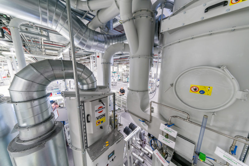 Industrial photography: Air filter installation on a machine in an industrial hall. The employees look small when you see them behind the large pipes on the filter housing.