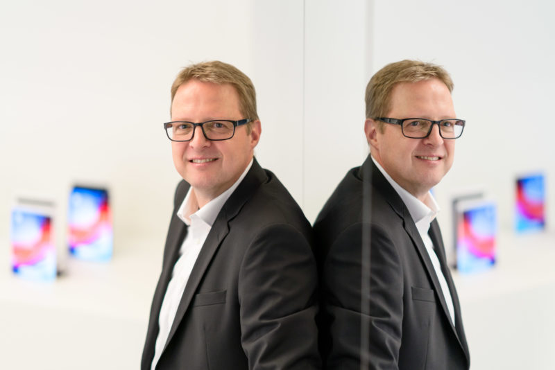 Portraitfotografie - Portrait eines Managers einer großen Softwarefirma: Bei vorhandenem Licht mit offener Blende fotografiert. Die Person spiegelt sich im Glas einer Scheibe.