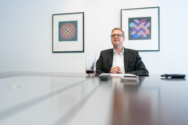 Portrait photography - Portrait of a manager of a large software company: The wide-angle lens used creates space and allows the use of reflections in the table where the person is sitting