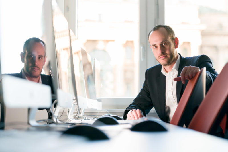 Mitarbeiterfotografie: Ein Mann sitzt in einem Computerschulungsraum. Sein Gesicht spiegelt sich in einem der Bildschirme.