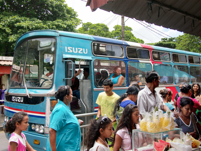 Reisefotografie: Mauritius: Gesichter und eine Modepuppe an einer vollen Busstation einer Hauptstraße.