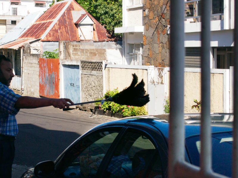 Reisefotografie: Mauritius: Ein Mann staubt mit einem großen Wedel sein Auto ab.