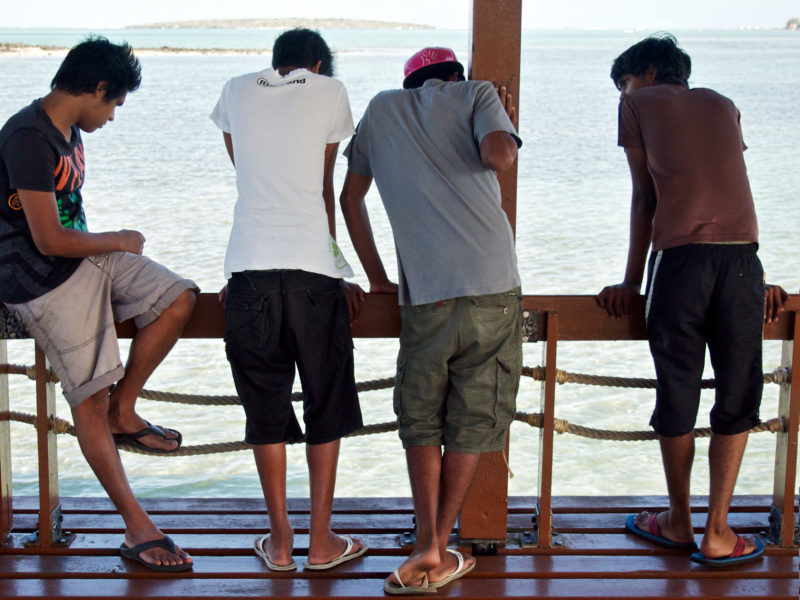 Reisefotografie: Mauritius: Vier Jungs in kurzen Hosen und T-Shirts beobachten von einem Steg aus die Fische im Wasser. 