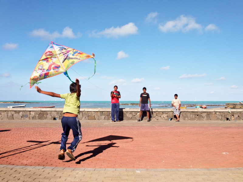 travel photography: Mauritius: Children play with a paper kite in the wind at the beach promenade of Grand Port.