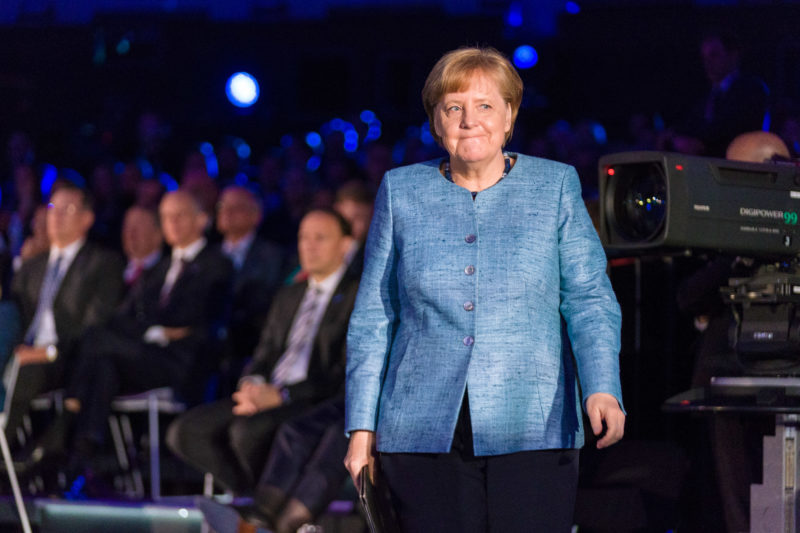 Editorial photography as event photography and fair photography: At the 350th anniversary ceremony of the Merck company in Darmstadt, Chancellor Angela Merkel goes to the lectern to give her speech. In the hand a book cover with the manuscript. In the background a camera for live transmission.