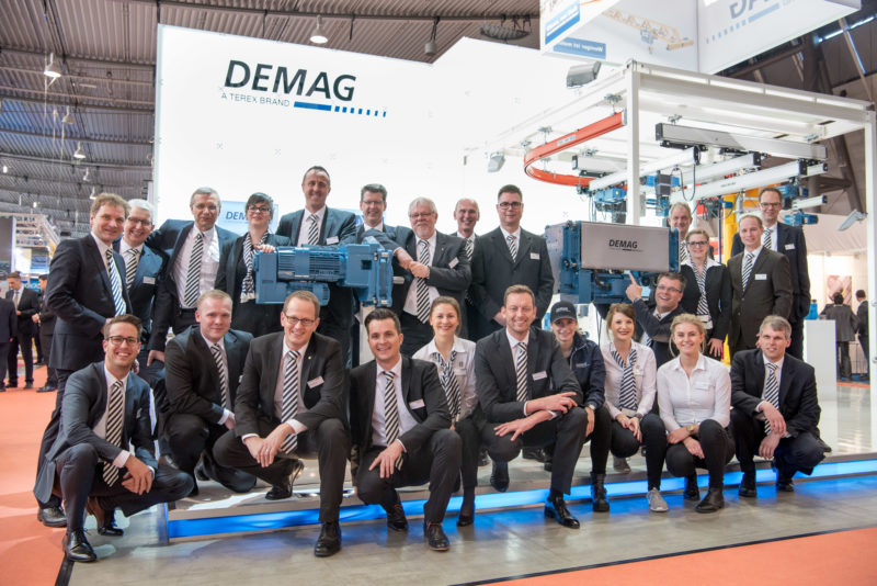 Group photo: Stand personnel of an exhibition stand in front of their brightly lit exhibition stand.