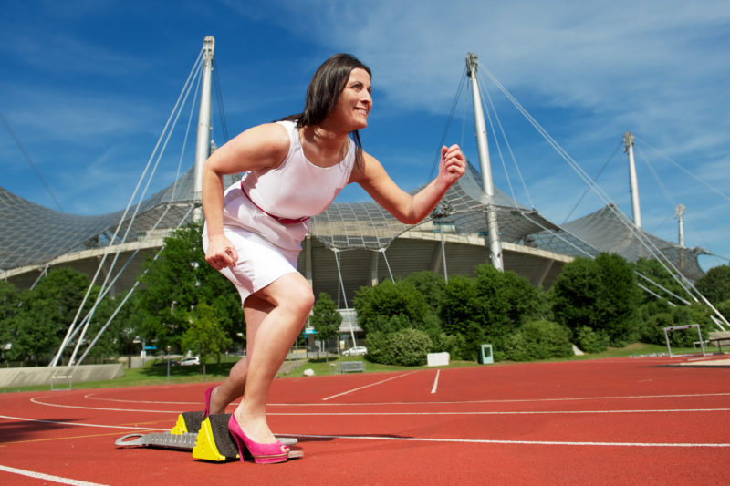 Mitarbeiterfotografie: Eine Mitarbeiterin einer Telekommunikationsfirma betreibt in ihrer Freizeit Sport. Auf dem Portrait steht sie bereit zum Start auf dem Startklotz einer Laufbahn.