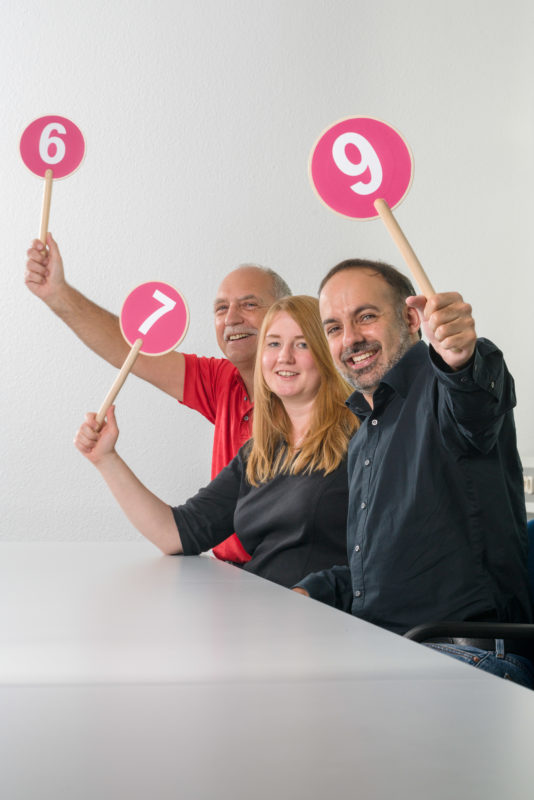 Mitarbeiterfotografie:  Eine Kollegin und zwei Kollegen posen mit Signalschildern in der Hand für deren Mitarbeitermagazin.