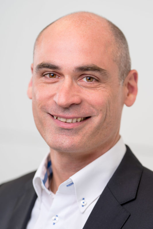 Portrait photography: Portrait of an employee illuminated with studio flash in front of a neutral background. The sharpness is almost exclusively on the eyes of the person by using the fully open aperture of a fast lens.