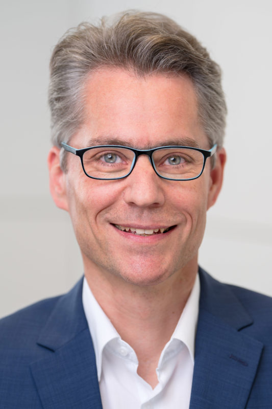 Portrait photography: Portrait of an employee illuminated with studio flash in front of a neutral background. The sharpness is almost exclusively on the eyes of the person by using the fully open aperture of a fast lens.