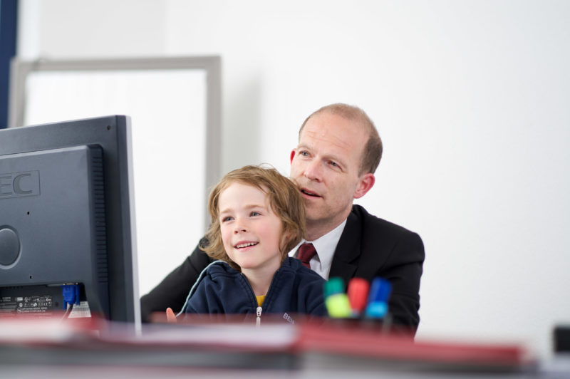 Reportagefotografie zum Thema Lernen und Bildung: Mitarbeiterportrait: Ein Vater zeigt seinem Sohn seiner Arbeitsplatz in einer Softwarefirma. Der Sohn freut sich.