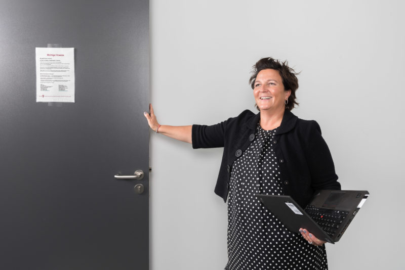 Employees photography: An employee with an opened notebook in her hand in the hallway of her company. She laughs as she opens a door.