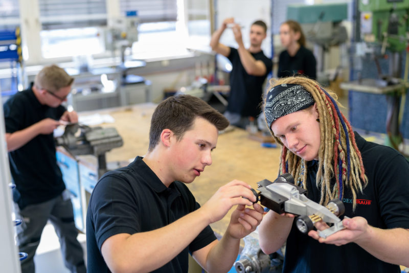 Industriefotografie: Auszubildende bei einem mittelständischen Maschinenbauer arbeiten an einem ihrer Lehrstücke, einem kleinen Rennwagenmodell aus Metall.
