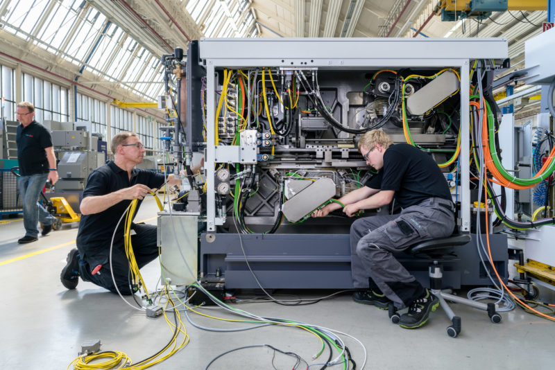 Industriefotografie: Bei einem mittelständischen Unternehmen verlegen zwei Mitarbeiter in der Fertigung Kabel in eine neue Maschine.