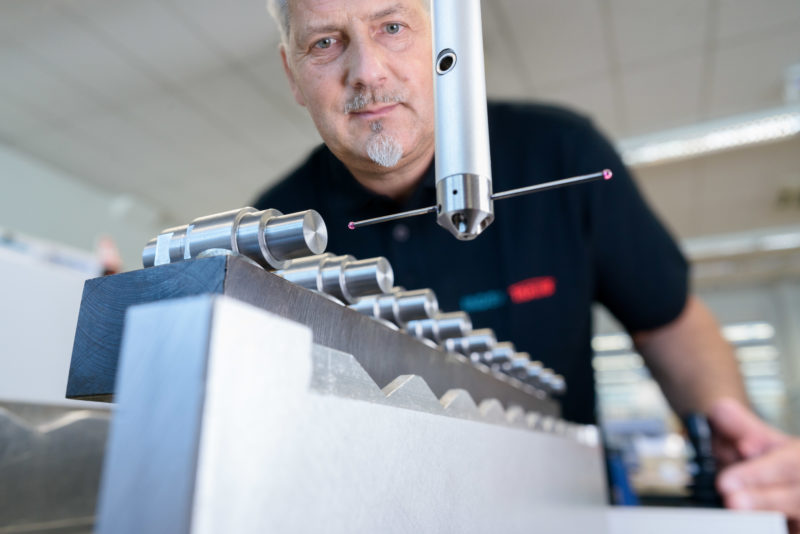 Industriefotografie: Ein Mitarbeiter in der Qualitätskontrolle eines mittelständischen Maschinenbauers vermisst Bauteile an einem Präzisionsmesstisch.