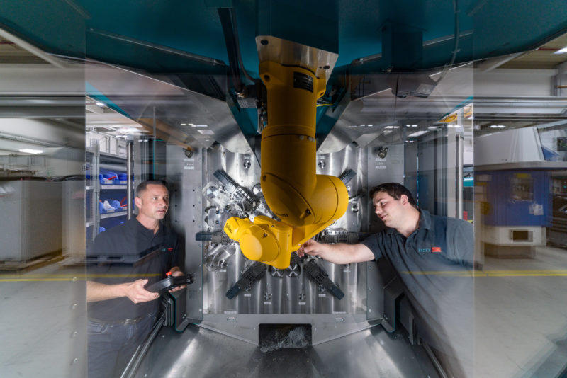 Industrial photography:  Employees testing a yellow robot arm in a new machine tool.