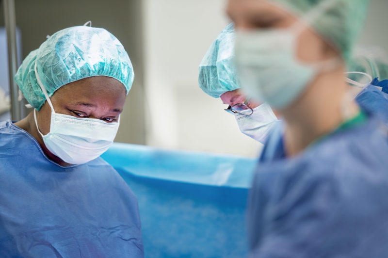 Medizinfotografie: Während einer Operation an einem Kreiskrankenhaus sieht man von der Chirurgin und ihrem Kollegen hinter deren Hygiene-Masken und Hauben nur die Augen.