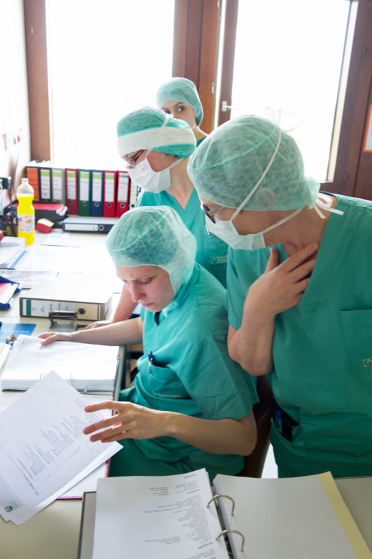 Medizinfotografie: Das Operationsteam muss nach jeder Operation eine umfangreiche Dokumentation erstellen. Sie drängen sich um den Schreibtisch im Dienstzimmer.
