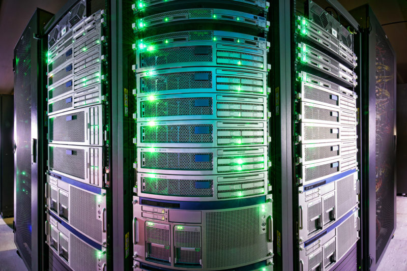 Industrial photography: Green illuminated server cabinet in a data center. The picture is taken in panorama technique to show the whole width of the servers standing next to each other.