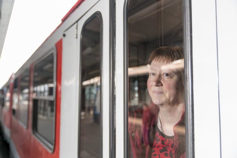 Mitarbeiterfotografie: Eine Pendlerin in der Bahn auf dem Weg zur Arbeit. Sie schaut in einem Bahnhof aus dem Fenster des Zuges.