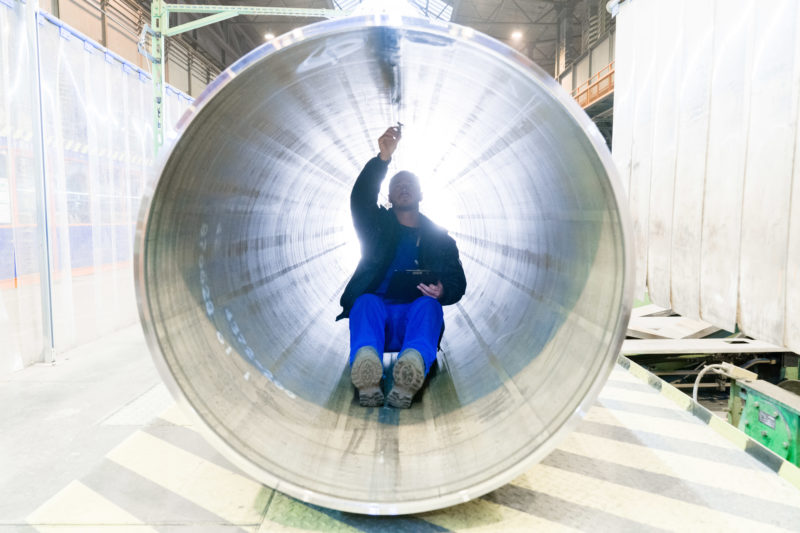 Industrial photography: In order to check the longitudinal weld seam of a pipe for a gas pipeline at a manufacturer of large steel pipes, an employee drives through the pipe on a rolling seat.