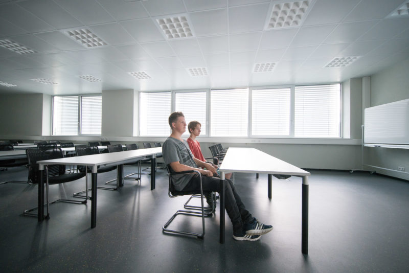 Reportagefotografie: Zwei Gymnasiasten sitzen in der ersten Stunde eines betrieblichen Praktikums etwas unsicher alleine in einem großen Unterrichtsraum und erfahren, was auf sie zukommt.