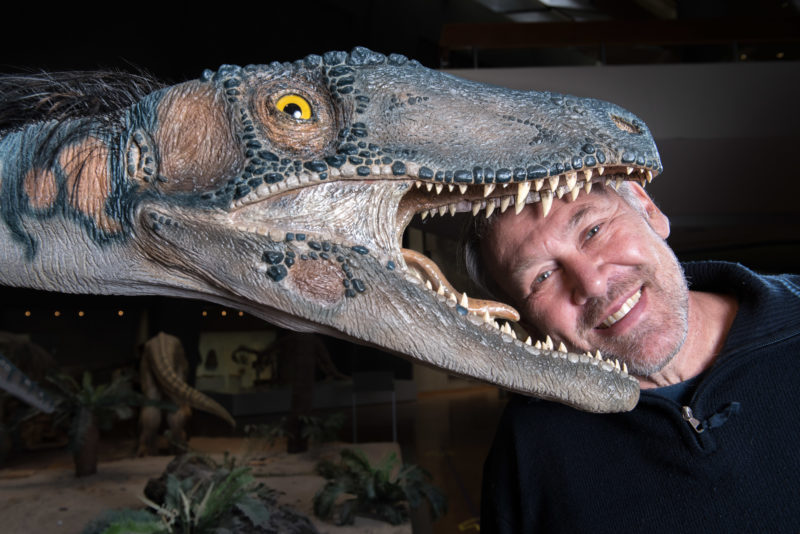Employees photography: A professor of geosciences laughingly stands behind a replica of a dinosaur so that his head seems to be in the mouth of the animal.